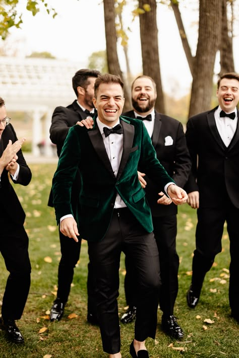 Group of groomsmen wearing black tux and groom is wearing green velvet jacket Green Velvet Bridesmaid Dresses With Groomsmen, Groomsmen Velvet Jacket, Velvet Green Tuxedo Wedding, Green Groom Suit Black Groomsmen, Black And Emerald Green Suit, Velvet Groomsmen Attire, Groom And Groomsmen Attire Green, Winter Groomsmen, Green Velvet Wedding