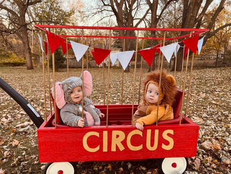 Twin toddlers dressed as circus animals (a lion and elephant) riding in a DIY cage made from a wagon. Red Wagon Halloween Costume, Halloween Costume Wagon Ideas, Diy Lion Cage Wagon, Circus Wagon Halloween, Lion Cage Circus Diy, Toddler Circus Costume, 2 Under 2 Halloween Costumes, Twin Family Halloween Costumes, Newborn Twin Halloween Costumes