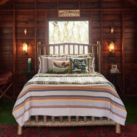 Inspired by the lined sleeping bags of the 1960s and ‘70s, this cozy comforter features an outer face of soft 100% cotton flannel emblazoned with multi-colored stripes in classic camp style. The reverse reveals Camp Wandawega outdoor scenes printed on 200-thread count cotton. An embroidered patch featuring camp mascot George completes a nostalgic journey back to nights of pine-scented breezes and rustling wildlife. Plush polyester fill provides lightweight warmth and machine washability. The Cam Bed For Cabin, Fishing Bed Rooms, Primitive Bedroom With Fireplace, Cowboy Roll Bed, Cabin Iron Bed, Vintage Cabin Fabric, Twin Bed Cabin Room, Rustic Cabin Twin Beds, Motor Home Bedding