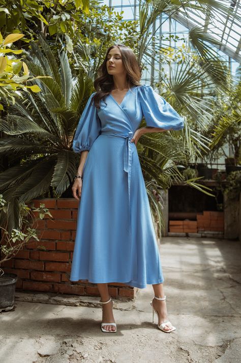 Embrace the beauty of summer with our Sky-Blue Puff-Sleeve Wrap Midi Dress. The sky-blue color radiates freshness and vibrancy, while the wrap design highlights your waist and creates a graceful silhouette. The playful puff sleeves and flowy skirt add a touch of whimsy, making this dress a delightful choice for outdoor gatherings and picnics. #dress #dresses #mididress #wrapdress #summerdress #weddingdress #eveningdress #dresslover #skyblue #womenwear #fashion Sky Blue Wedding Guest Dress, Light Blue Dress With Sleeves, Sky Blue Colour Dress, Sky Blue Dress Outfit, Blue Dress Sleeves, Pastel Color Dresses, Flowy Wedding Guest Dress, Blue Dress Modest, Pastel Dress Outfit