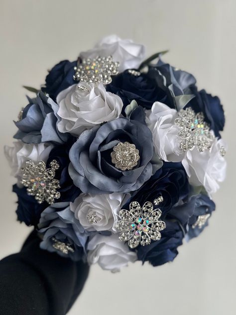 Handmade quinceañera bouquet with navy blue, dusty blue and white color shade of roses. Finished off with silver brooches.  *Please note brooches can change in style based on availability*   Decor can be changed upon request.  *This is a made to order bouquet* Wedding Bouquets Dark Blue, Navy Blue Debut Theme, Navy Blue Quince Bouquet, White Quinceanera Bouquet, Navy Blue Quinceanera Ideas Decor, Dark Blue Quinceanera Theme, Navy Quince, Quinceanera Navy Blue, Navy Blue Quinceanera Ideas