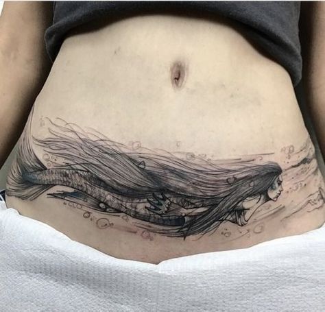 For the person who loves mermaids comes this stunning mermaid tattoo for tummy tuck scars! The mermaid is created in black ink and extends throughout the width of the stomach and onto the hip area. The mermaid’s long, flowing hair expertly hides all elements of the scar, while the bubbles and flowing water add to the final look. Lower Abdomen Tattoo, C Section Scar Tattoo, Lower Belly Tattoos, Abdomen Tattoo, Side Stomach Tattoos, Lower Stomach Tattoos, Tummy Tattoo, Tattoo Over Scar, Stomach Tattoos Women