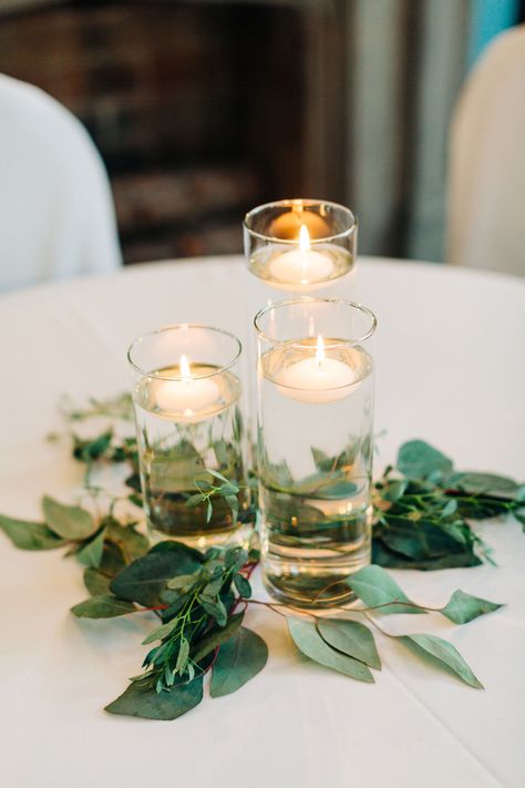 Floating candles with greenery wedding reception Floating Candles For Wedding, Floating Candle Centerpieces Eucalyptus, Floating Tea Candle Centerpieces, Wedding Table Floating Candle Centerpieces And Eucalyptus, Simple Cheap Centerpieces Wedding, Inexpensive Reception Centerpieces, Candles In Glass Cylinders Wedding, Candle Round Table Centerpiece, Floating Tea Lights Wedding