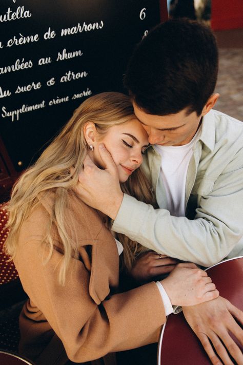 A man and a womans sitting at a table while she rests her head on his shoulder and has his hand on her cheek, up close. Couples engagement photo shoot in Paris France. Head Resting On Lap Pose, Couple Leaning On Shoulder Reference, Resting On Shoulder Couple, Head In Lap Couple, Laying Head On Shoulder Couples, Resting Head On Shoulder Couple, Resting Head On Shoulder Reference, Head Resting On Shoulder Reference, Head On Shoulder Couple