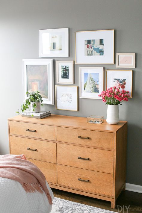 Gallery wall over a dresser. This gray guest bedroom may have a neutral color, but it's full of personality. With floral pillows, brass accents, and a gorgeous gallery wall. Love the dark gray paint color too, Benjamin Moore's Chelsea Gray #graybedroom #guestroom #floral #femininebedroom #blush #brass #guestbedroom Bedroom With Blush Accents, Gray Guest Bedroom, Dresser Wall Decor, Stairway Gallery Wall, Bedroom Decor For Women, Chelsea Gray, Feminine Bedroom, Gray Paint, Master Decor