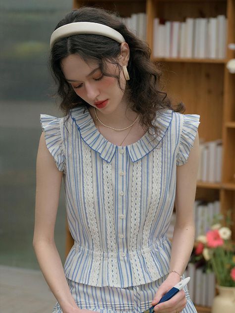 This product, the Flying Sleeve Cotton Shirt, showcases a charming combination of vintage-inspired elements and modern tailoring. It features ruffled flying sleeves and a delicate lace trim along the front, adding a touch of softness and femininity. The fitted waist enhances the silhouette, making it a versatile piece for both casual and formal occasions. - This Flying Sleeve Cotton Shirt incorporates playful ruffled sleeves that add movement and a vintage charm to the design.- It includes intricate lace detailing along the placket, which enhances the shirt's elegant and sophisticated appeal.- The shirt is tailored to emphasize the waist, offering a flattering fit that pairs well with both skirts and trousers.- Crafted from pure cotton, this shirt promises both comfort and durability, Flowy Shirt Outfit, Gingham Top Outfit, Dubai Outfit, Modern Tailoring, Indian Dresses For Women, Traditional Dresses Designs, Fashion Silhouette, Myanmar Traditional Dress, Myanmar Dress Design