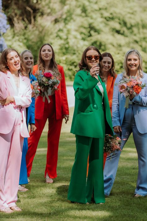 6 bridesmaids playing outdoor garden games in colourful suits. Pink, blue, red, green, orange and light blue Non Formal Wedding Attire, Bridesmaid In Suits, Pant Suit Bridal Party, Bridal Party In Suits, Bridesmaid In Suit, Wedding Guest Dress Colorful, Fun Wedding Outfits, Colorful Fun Wedding, Festival Themed Wedding Guest Outfit