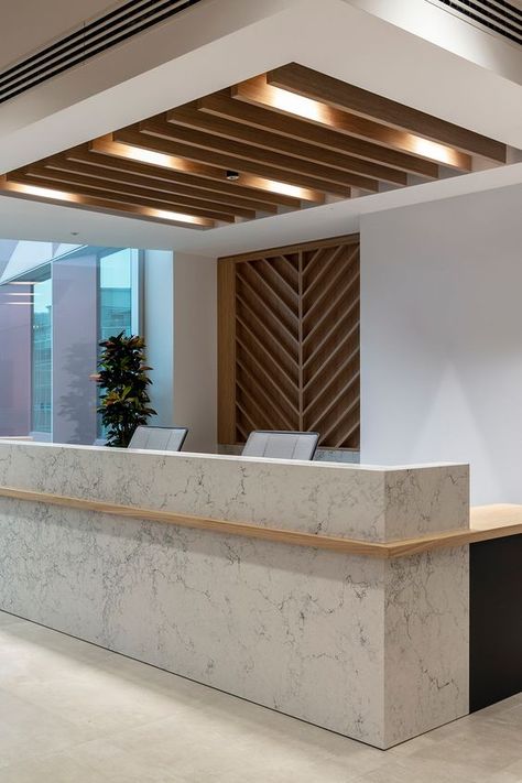 An office recpetion desk with marble used as a hard wearing and high quality frontage and an oak worktop mirroring the timber feature ceiling above. Office Ceiling Design Modern, Reception Office Ideas, Reception Ceiling Design, Modern Office Reception Design, Office Reception Desk Designs, Marble Reception Desk, Unique Reception Desks, Office Reception Counters, Modern Reception Desk Design