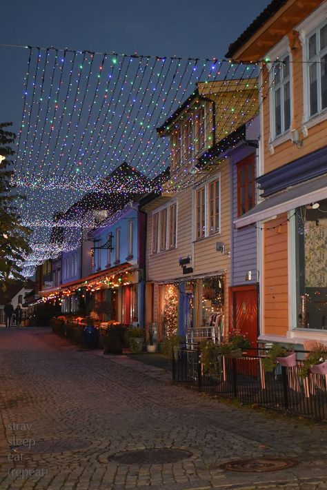 Twinkle lights shimmer over a cobblestone walkway lined with colorfully painted buildings. Norway City, Norway House, Stavanger Norway, Colourful Buildings, Norway Travel, Stavanger, Dream Holiday, Winter Pictures, Winter Aesthetic