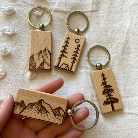 There are 4 wood rectangular keychains with woodburned designs. There is a vertical mountain, horizontal mountain, a cedar tree and a camping themed one. Woodburning Keychain Ideas, Wood Burned Keychain Ideas, Wood Burning Keychain, Woodburn Keychain, Wood Burning Keychain Ideas, Wood Keychain Ideas, Wooden Keychain Ideas, Camping Keychain, Craft Stall Display