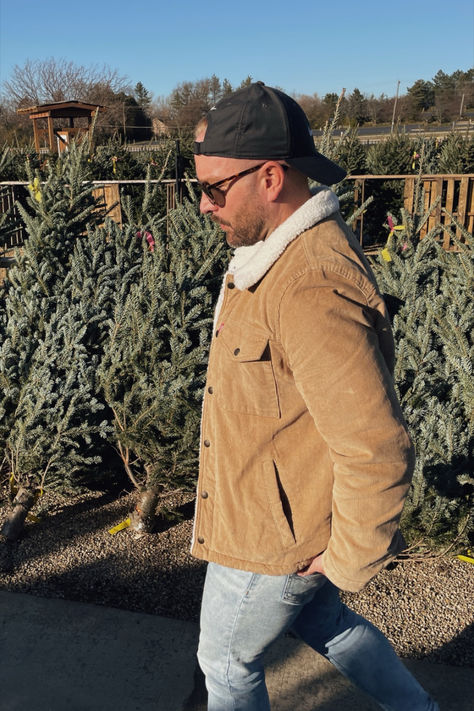 Man walking in front of a row of fresh cut christmas trees wearing a tan corduroy jacket, light wash jeans and a backwards black hat. Street Fashion Men Streetwear, Men Streetwear, Winter Outfits Men, Trucker Jacket, In The Winter, Basic Tee, Mens Streetwear, Men Winter, Winter Outfit