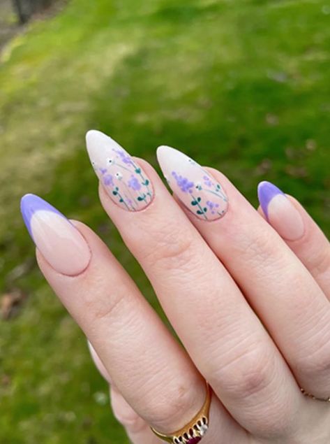 Almond-shaped nails with a clear base, adorned with delicate lavender flower accents and soft pastel purple tips, perfect for a fresh spring look. Lilac Nails Almond Short, Nail Ideas Almond Shape Purple, Nails With Lavender Flowers, Lavender Flower Nail Designs, Lavender Flower Nail Art, Grad Nails Purple, Lavender Floral Nails, Lavender Design Nails, Lavender Acrylic Nails Almond