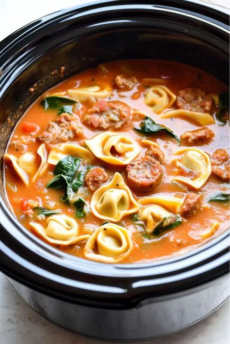 A hearty Italian slow cooker soup with cheese tortellini, sausage, carrots, spinach, and tomatoes in a crockpot, simmering in a creamy tomato broth. Crockpot Soup With Spinach, Crockpot Italian Sausage Tortellini Soup, Slow Cooker Sausage Soup, Slow Cooker Chicken Tortellini Soup, Tortellini Slow Cooker Recipes, Slow Cooker Tomato Tortellini Soup, Tomato Tortellini Soup Crockpot, Crockpot Tortellini Recipes, Slow Cooker Creamy Tortellini Soup