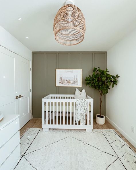 Green feature wall with wicker light fixture and textured rug; plant, white crib, boho art Olive Green And Grey Nursery, Sage Green Nursery With White Crib, Green Feature Wall Nursery, Sage Green And White Nursery, Green White Nursery, Nursery Ideas White Crib, Plants For Nursery, White Crib Boy Nursery, Nursery With White Crib