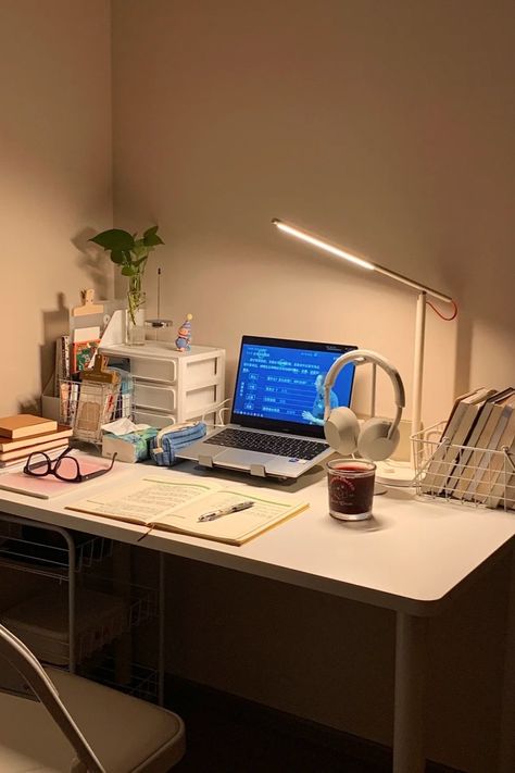 A minimalist study desk setup with a laptop, open notebook, reading lamp, headphones, and a calming candle. The desk also includes books, a plant, and organizational drawers, creating a warm and inviting space perfect for studying or working Laptop Only Desk Setup, Laptop Desk Setup Small Spaces, Small Cozy Desk Setup, Uni Desk Setup, Desk Organization Laptop, Laptop Setup Work Spaces, Academia Desk Setup, Simple Desk Organization, Small Desk Setup Ideas