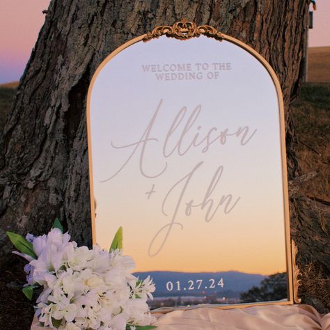 "Please send us a direct message with any questions about design, products, shipping, or rush orders! ABOUT THE MIRROR The ambiance of your wedding won't be complete without the finishing touch of our stunning Welcome Sign on a Gold Arch Mirror. A wedding welcome sign is a must-have addition to your celebration. Placed near the entrance of your wedding ceremony or reception, it acts as a warm and inviting greeting for your cherished guests. But it's more than just a greeting; it's a canvas for creativity and information-sharing. This elegant, custom wedding accent presents itself in the popular arch shape and is decorated with timeless fleurons on the bottom left and right corners as well as a larger fleuron on top center. The frame is coated with metallic gold paint that has micro-shimmer Circle Mirror Welcome Sign Wedding, Wedding Entrance Sign Mirror, Arch Mirror Wedding, Welcoming Board, Welcome Sign Mirror, Gold Mirror Wedding, Large Gold Mirror, Gold Arch Mirror, Mirror Wedding Signs