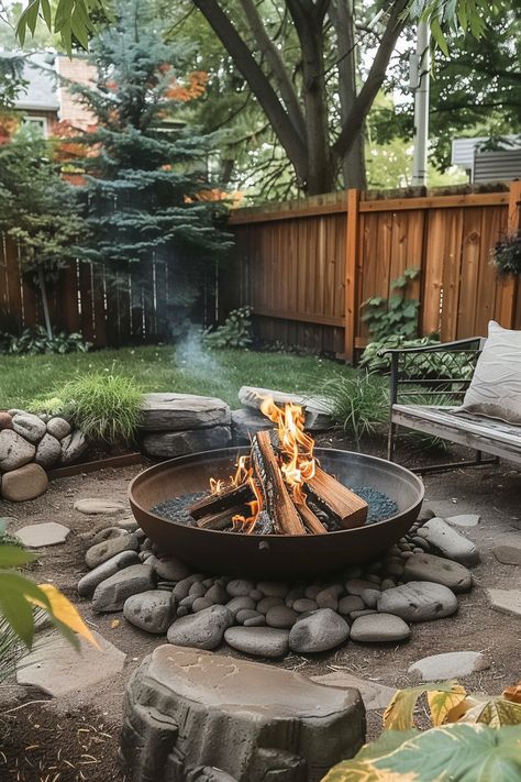 A cozy backyard with a fire pit surrounded by rocks, a wooden fence, and lush green trees and plants, perfect for relaxing outdoors. Outside Rock Fire Pit Ideas, Diy Fire Pit Sitting Area, Circle Fire Pit Area Diy, Pea Gravel Fire Pit Area Diy, Gravel Bonfire Pit, How To Level Ground For Fire Pit Area, Creekside Fire Pit, Fire Pit With Half Wall, Cool Backyard Features