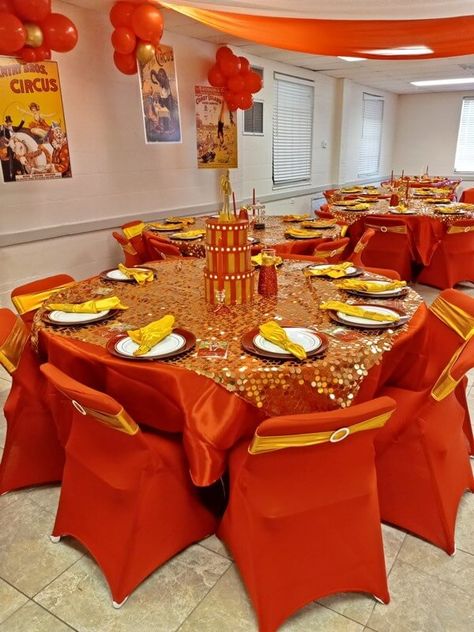 Add imperial charm to your circus themed party décor by dressing your tables with orange tablecloths and gold sequin overlays. Create a presentable place setting by arranging yellow napkins with orange chargers and white plates as well as opt for red taper candles to enhance your display. Also, adorn your chairs with orange covers and gold sashes and decorate your empty walls with gold and orange balloons. Lastly, cover your ceiling with orange and white drapes for a cohesive appeal. Red And Yellow Table Setting, Orange And Gold Decorations, Orange And Yellow Party Decorations, Iftaar Ideas, Red Taper Candles, Orange Charger, Yellow Party Decorations, Yellow Dinner, 75 Birthday