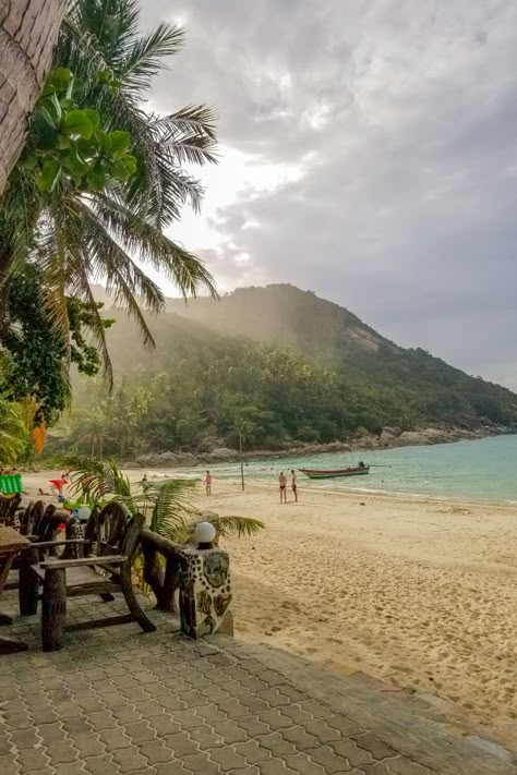 A moody view of the changing weather on one of the best beaches in Koh Phangan. This tropical island view showcases a waterfront restaurant that sits on a white sandy beach with the crystal clear turquoise water of the Gulf of Thailand. Long tail boats, the typical Thailand boat, sit in the water with palm trees and the lush jungle in the background. Phuket Thailand Beach, Koh Samui Beach, Travel Aesthetics, Thailand Vacation, Thailand Adventure, Full Moon Party, Thailand Trip, Thailand Backpacking, Thailand Travel Tips