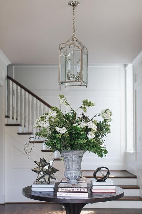 An arch lantern hangs over a styled round black wood entry table. Round Table Hallway, Round Entryway Table Styling, Hallway Round Table, Round Entry Table Styling, Entryway With Round Table, Round Foyer Table Decor, Round Foyer, Foyer Table Decor, Entrance Table Decor