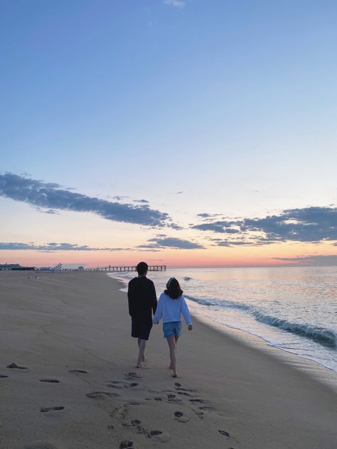 A couple is walking down the shore during sunrise. There are cotton candy skies + a boardwalk in the background Picture Sweet Couple, Beach Dating Aesthetic, Relationship Beach Aesthetic, Morning Date Aesthetic, Sunrise Date Ideas, Sweet Pictures Of Couples, Beach Date Aesthetic Couple, Beach Dates Couple, Holiday Aesthetic Summer Couple