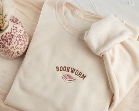 Embroidered Bookworm Sweatshirt Stay cozy and fun with our uniquely embroidered sweatshirt! Made with love and THOUSANDS of threads! -Unisex Size (Please see the size chart for more details that can be found in the photos section)  We recommend comparing your favorite sweatshirt to our size chart to find the best size for you! Unisex Crewneck -50% cotton 50% polyester -Super soft -Pre-shrunk -Unisex -Design size is 3''-4"  Thread: We use the best quality threads for our embroidery designs. Aesthetic Embroidered Sweatshirt, Book Sweatshirts, Bookworm Sweatshirt, Etsy Sweatshirts, Sweatshirts Aesthetic, Embroidered Book, Gifts Book, Sweatshirt Embroidery, Bookclub Gifts