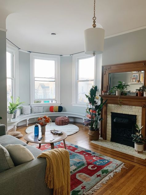 This shared San Francisco apartment has a huge bay window, black and white tiled kitchen flooring, three fireplaces, and stained glass windows. It can best be described as a colorful, maximalist urban jungle. #maxmalist #rentalhomedecorating  #renterfriendlyhacks #livingroomdecor #livingroomideas #apartmentideas Chicago Apartment Interior, San Francisco Apartment Aesthetic, San Francisco Houses Interior, San Francisco Apartment Decor, Boston Apartment Aesthetic, Curved Window Seat, Chicago Apartment Aesthetic, Sf House, Round Walnut Coffee Table