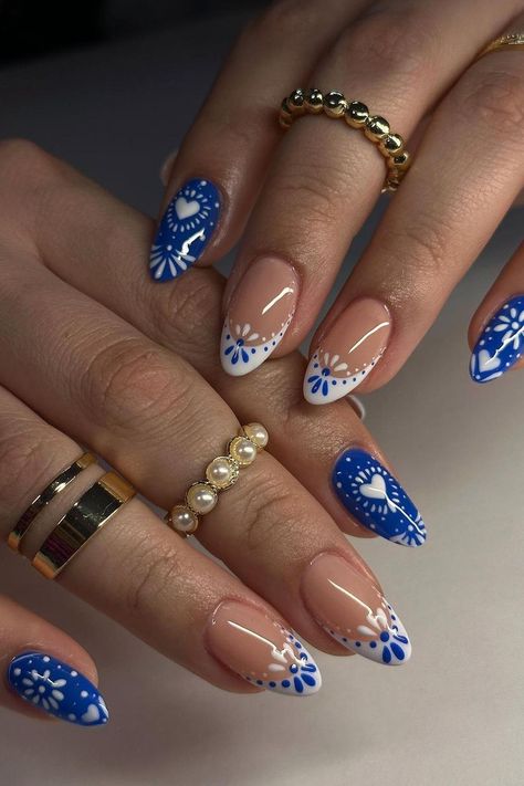 These almond-shaped nails are a playful mix of summer vibes with a contrasting design. The vibrant blue base pops with white floral patterns and heart shapes, while the clear nails are elegantly simple with a hint of white floral art and subtle line accents. The pairing of bold and subdued creates a lovely and engaging aesthetic perfect for sunny days.  // Photo Credit: Instagram @chibimoon.nails Oval Shaped Summer Nails, Nail Design Clear Base, Nails Almond Short Design, Blue Nails Aesthetic Design, Fake Nail Design Ideas, China Dish Nails, Short Almond Nails Elegant, Subtle Almond Nails, Summer Subtle Nails