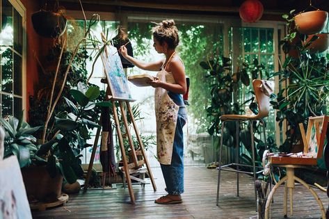 Indoor shot of professional female artist painting on canvas in studio with plants.