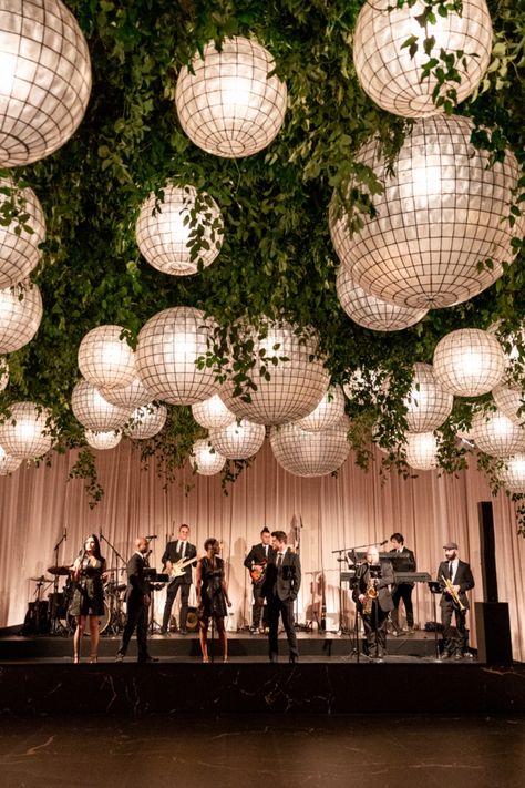 This breathtaking ceiling installation features large white lanterns woven through lush greenery, creating an enchanting garden-like atmosphere indoors. The perfect backdrop for an unforgettable wedding or event, combining natural elements with modern design.  #WeddingDecor #LanternLighting #GardenWedding #LuxuryEvent #ModernWeddingDesign #EventInspiration #IndoorGarden Disco Garden Wedding, Wedding Ceiling Installation, Indoor Reception Decorations, Reception Ceiling Design, Ceiling Installation Wedding, Event Lounge Area, Greenery Ceiling, Indoor Garden Wedding Reception, Hanging Lights Wedding