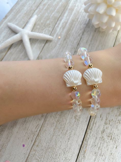 ⭐️⭐️ IRIDESCENT GLASS BEAD CLAM BRACELET ⭐️⭐️ Add mermaid vibes to your day with this iridescent clam bracelet! The listing is for one bracelet, images showing more than one are an example of how they would look stacked with other bracelets. Please choose your size from the drop-down menu. If you do not see your size there, send me a message with your size and I will be happy to make it for you. ♥ ITEM DETAILS ♥ 8mm Clear glass iridescent beads 4mm Gold plated beads 14mm Acrylic clam bead Sturdy stretchy elastic Your bracelet will come in a drawstring bag, ready to be gifted. If you are purchasing multiple bracelets and would like them packaged separately, please leave me note at checkout. All sales are final. If you have any questions, please feel free to message me. ♥ CARING TIPS ♥ Keep Beach Vibe Bracelet, Shell Bead Bracelet, Bracelet Images, Beads Craft Kids, Bracelets Rainbow, Mermaid Vibes, Multiple Bracelets, Mermaid Bracelet, Mermaid Jewelry