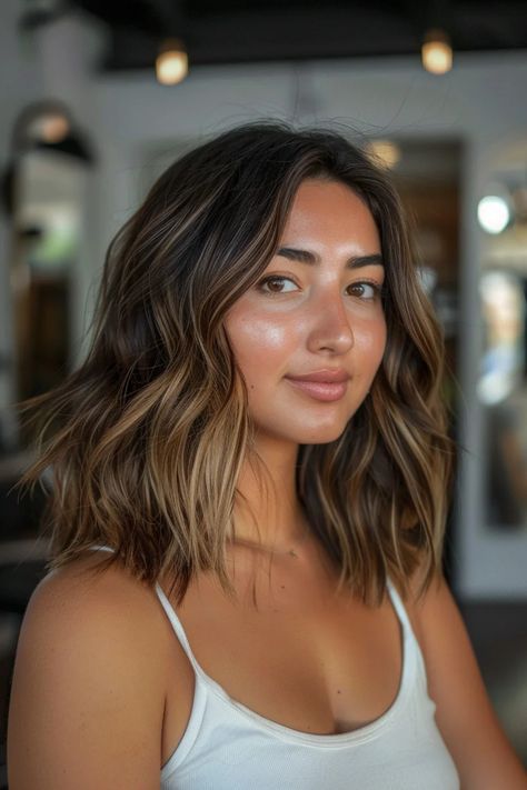 A woman with wavy brunette hair and a white tank top smiles softly, with a blurred indoor background. Golden Caramel Highlights, Dark Caramel Balayage, Bold Highlights, Blonde Transformation, Brunette Roots, Dark Golden Blonde, Darker Hair, Natural Brown Hair, Brown Hair With Caramel Highlights