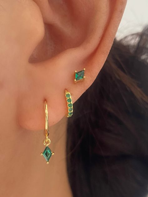 Indulge in elegance with our stunning Emerald Green Cubic Zirconia dangle drop earrings set. Whether you wear them as a trio or individually, these pieces exude sophistication. Crafted with premium brilliant cubic zirconia, they sparkle from every angle. 3 Pairs Set comes with a Gift Box A. Dangle Earrings. • Materia: 18k Gold plated on 925 Sterling Silver, AAAAA Cubic Zirconia• measurements: 19mm in length, Hoop inner diameter: 8.5 mm B. Huggie• Materia: 18k gold plated on 925 sterling silver, 3 Set Earrings Ideas, Green Earings Piercings, Gold And Emerald Earrings, Gold And Green Earrings, Classy Earring Stack, Elegant Piercings Ears, Ear Piercing Set Up, Stacked Ear Lobe Piercing, Green Jewerly