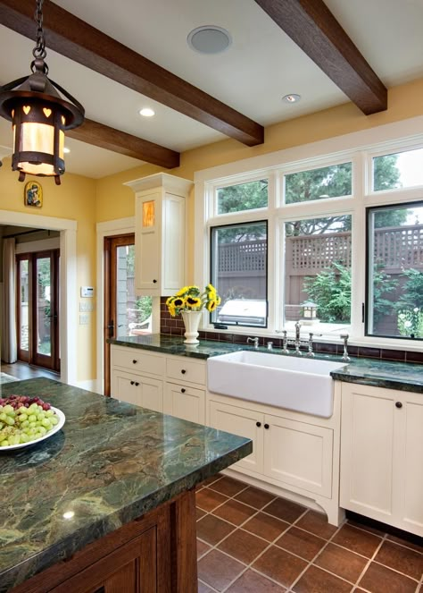 Deep forest green marble countertops add gorgeous color to this kitchen design. A large, white farmhouse sink is fitted into the counter below the natural light of a trio of windows. Exposed wood ceiling beams compliment the wood finish of the island fixed under the lantern pendant light with heart trim. Green Kitchen Countertops, Countertop Concrete, Green Countertops, Replacing Kitchen Countertops, Marble Countertops Kitchen, Craftsman Kitchen, Kabinet Dapur, Kitchen Countertop Materials, Kitchen Wall Colors