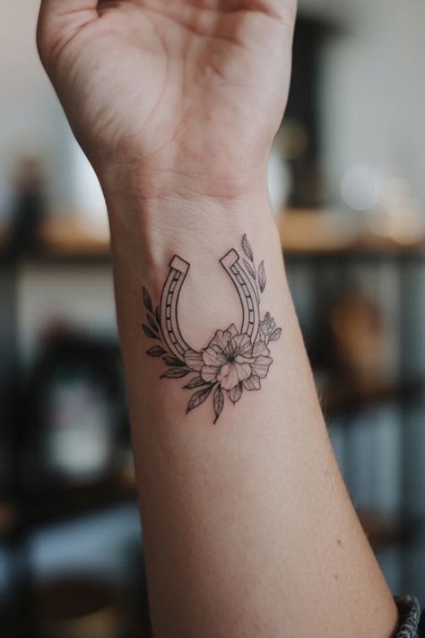 Horseshoe tattoo with floral design on a person's wrist. Horse Shoe Tattoo Traditional Design, Feminine Horseshoe Tattoo, Mother Daughter Tattoos Western, Simple Horse Shoe Tattoo, Horseshoe And Flower Tattoo, Cowboy Boots Tattoo Ideas, Cool Horse Tattoos, Tiny Tattoos Western, Small Horse Shoe Tattoos