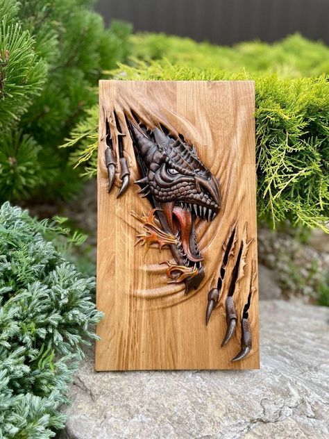 A wooden painting depicting a dragon is a true work of art that combines the natural beauty of wood with the craftsmanship of carving. The painting is made from high-quality wood, carefully treated and polished to create a smooth surface. It features a dragon -- a mythological creature symbolizing strength, wisdom, and protection. The carving impresses with its detail: each scale on the dragon's body, its sharp claws, and expressive face create a sense of realism and dynamism. The background of the painting is also decorated with carved elements, adding depth and volume to the composition. The dragon breaks through the base of the image with its claws, making the painting even more realistic. The dragon's eyes are meticulously carved from wood, appearing lifelike and adding even more expre Cargo Ideas, Viking Wood Carving, Dragon Faces, Unique Wood Carving, Wooden Dragon, Chainsaw Wood Carving, Carved Wooden Animals, Sharp Claws, Mythological Creature