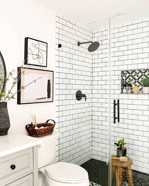 White subway tile shower is finished with a black faucet kit and seamless glass enclosure. A wooden stool is placed in the shower on top of black hexagon floor tiles. Black Hexagon Tile Shower, Subway Tile With Black Grout, White Tiles Black Grout, Tile With Black Grout, Black Tile Bathroom, Hexagon Tile Bathroom Floor, Mosaic Tile Bathroom Floor, White Subway Tile Shower, Bathroom Shower Floor