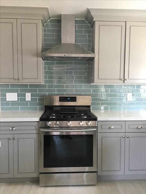 Blue glass tile backsplash with gray cabinets and white quartz countertops and range hood Luxury Grey Kitchen, Blue Glass Tile Backsplash, Backsplash Blue, Gray Kitchen Backsplash, Blue Backsplash Kitchen, Glass Tile Backsplash Kitchen, Light Grey Kitchen Cabinets, Blue Glass Tile, Light Grey Kitchens