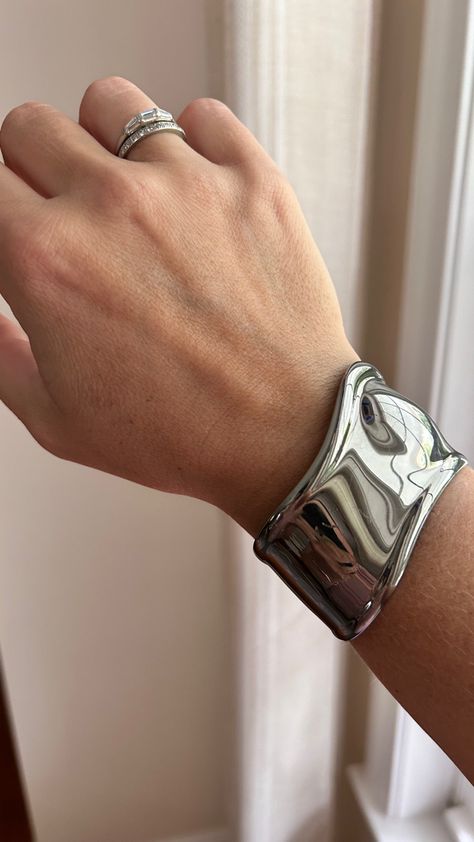 A photo of a white woman’s wrist by a window. She is wearing a wide, sculptural cuff bracelet in ruthenium, a dark silver metal, and two diamond rings on her ring finger. Tiffany Silver Cuff Bracelet, Bone Bracelet Tiffany, Tiffany Bone Cuff Outfit, Tiffany Bone Cuff Bracelet, Tiffany And Co Elsa Peretti, Tiffany Cuff Bracelet, Bone Cuff Elsa Peretti, Tiffany And Co Jewelry Aesthetic, Elsa Peretti Bone Cuff