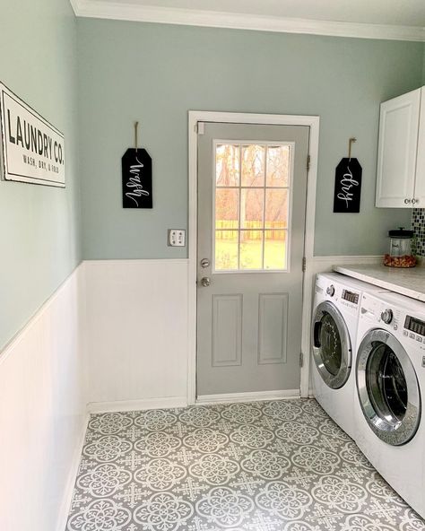 Gray door is fitted into a light green wall with white beadboard wainscoting. A white washer and dryer are placed next to the door in this laundry room featuring white and gray mosaic flooring. Seafoam Green Laundry Room, Eucalyptus Laundry Room, Laundry Room Gray Walls, Laundry Room With Beadboard, White Cabinets In Laundry Room, Pale Pink Laundry Room, Green Laundry Room Design, White Beadboard Laundry Room, White Tile Green Wall Bathroom