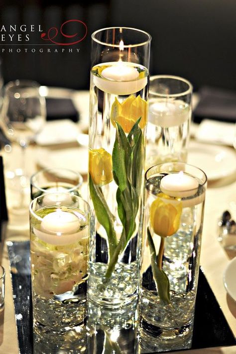 pretty yellow floating candle centerpiece in staggered cylinders Daffodil Wedding Centerpieces, Yellow Centerpieces, Wedding Ceremony Songs, Floating Candle Centerpieces, Tulip Decor, River Wedding, Tulip Wedding, Elegant Wedding Centerpiece, Candle Centerpiece