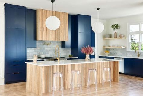 The light wood fluting on the island and range hood is a fresh, attractive contrast to this kitchen's vibrant navy cabinetry. Large windows above one of the sinks (there are two) welcome in lots of light. Blue White Wood Living Room, Navy And Wood Kitchen, Kitchen With Big Island, Village Family, Navy Kitchen, Interior Design Gallery, Mediterranean Kitchen, Chinoiserie Decorating, Kitchen Paint Colors