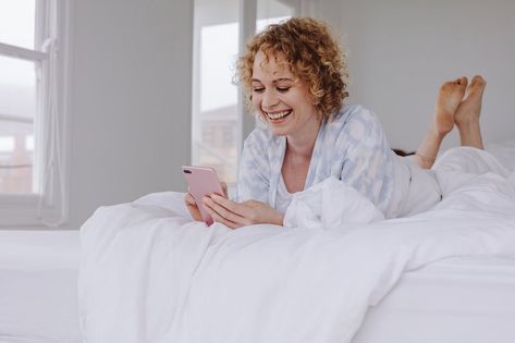 Happy woman lying on bed checking her cell phone. Woman using her mobile phone lying in bed after waking up in the morning. Waking Up In The Morning, Person Photo, Lying In Bed, Bed Legs, Smiling Woman, Happy Woman, Anatomy Poses, Pose References, Calligraphy Fonts