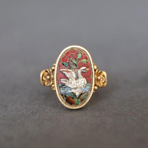 A stunning antique micromosaic ring, likely of Italian origin, dating to the Victorian era (1837-1901). The ring features an oval-shaped mosaic created from tiny, multicoloured glass tiles (tesserae) depicting a white swan on the water with foliate flourishes. Crafted in  18ct yellow gold, the band and bezel are embellished with design elements including a millegrain border, flower motifs to the shoulders and a split shank. Perfectly sized for the pinky, this well-preserved ring is truly a rare Antique Rings Victorian Gold, Victorian Wedding Ring Antique Jewelry, Vibtage Rings, Antique Silver Ring, Vintage Ring With Bezel Setting, Artistic Engagement Rings, Victorian Gold Jewelry, Micromosaic Ring, Victorian Wedding Rings