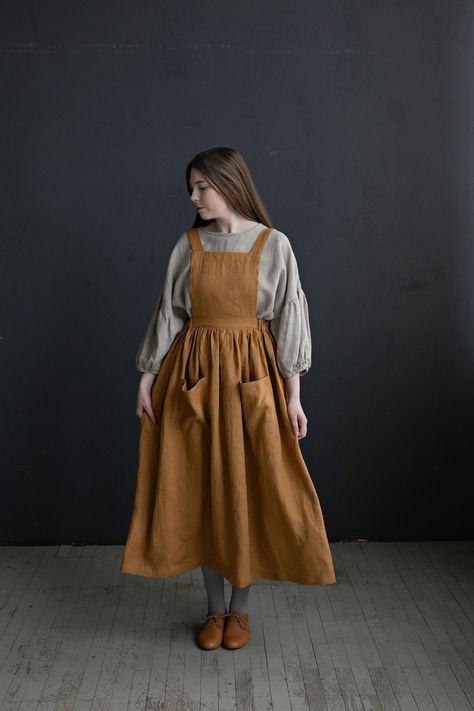 Cottage dress is made from 100% soft and washed linen. Details: - Colour: Mustard - Composition: 100% Oeko-Tex certified linen - Pockets - Cross back - Length - 124 cm (49 inches) - Adjustable with buttons - Elastic Waist - Medium weight linen - Linen care: machine wash gentle; tumble dry low, ironing optional - The price is for one pinafore dress, other pictured items are not included Victorian Apron, Victorian Aprons, Linen Pinafore Dress, School Uniform Dress, Cottage Dress, Homemade Dress, Farm Dress, Linen Pinafore, Pinafore Apron