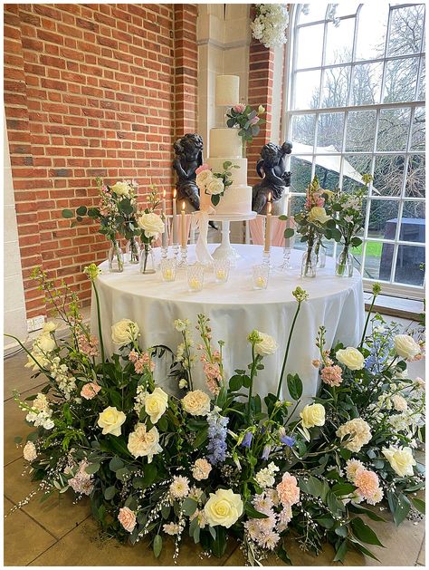 pastel pink, blue, ivory creams flower meadows at the bottom of a round cake table, bud vases on a cake table, beautiful cake table with flower meadows around it. Flower Meadows, Spring Flower Wreath, Wedding Flower Packages, Flower Meadow, Open Day, Wedding 2025, Wedding Cakes With Flowers, Flower Packaging, Meadow Flowers