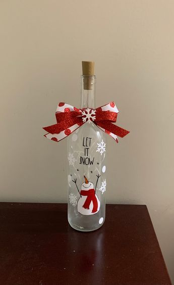 Get festive by adding a wine bottle light to your Christmas decor! LED battery operated Christmas wine bottle lights.   "Let it Snow " Snowman design. Extra batteries included These make great gifts!  Made out of clear wine bottle, with vinyl and frosted finish. Decorated with ribbon. If ordering multiple items, please send me a message and I will create a custom listing for you to bundle and save on shipping. Light Up Wine Bottles Diy Christmas, Holiday Painted Wine Bottles, Diy Painted Bottles Ideas, Christmas Decorated Bottles, Gingerbread Wine Bottle, Christmas Crafts With Wine Bottles, Christmas Bottle Painting Ideas, Christmas Glass Bottle Crafts, Wine Bottle Snowman Crafts Diy