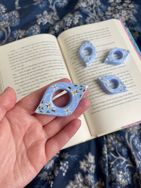 A great gift for any avid reader or book lover, this thumb ring page holder is hand-crafted from air dry clay and painted Bridgerton-blue with Featherington-yellow flowers and golden bees to bring a bit of spring romance to your reading experience. This book accessory will allow you to read comfortably with one hand and, for anyone looking for some support, it should help as an aid to make reading more accessible (to note: this particular listing isn't designed to order, but if you have specific Air Dry Clay Tealight Holder Diy, Polymer Gift Ideas, Book Ring Holder, Air Dry Clay Page Holder, Thumb Page Holder, Cloud Clay Art, Clay Book Page Holder, Wood Projects Cute, Small Diy Clay Ideas