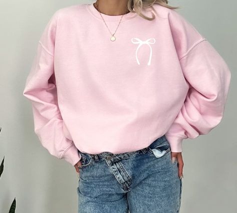 Step into the world of effortless chic with our Bow Coquette Sweatshirt, a garment that epitomizes the fusion of comfort and style. The Pink Ribbon Coquette Bow Minimalist Crewneck is more than just a piece of clothing; it's a statement of understated elegance. Designed with a keen eye for the aesthetic, this Plain Bow Sweatshirt features a delicate, trendy  bow that adds a touch of whimsy to your everyday wardrobe. Each Coquette Sweater is meticulously crafted to ensure you stand out in the most sophisticated way possible. ------------------------------------------------------------------------------------- 8.0 oz., 50/50 pre-shrunk cotton/polyester Softer air-jet spun yarn 1x1 athletic rib knit collar, cuffs and waistband, with spandex Double-needle stitched cuffs and waistband Tearaway Clothes With Bows, Bow Clothing, Minimalist Crewneck, Coquette Sweatshirt, Coquette Sweater, Bow Outfit, Bow Sweatshirt, Trendy Bows, Coquette Bows