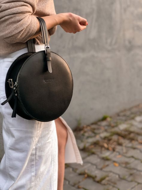 "Leather circle crossbody bag with a convenient harness for carrying on the shoulder and a handle for carrying the bag in hand.  There is a pocket on the outer back of the bag.  Material: Italy Leather  Color of the leather: black Hardware: Italian fittings of high quality Hardware color: nickel  Overall size: diameter  9.44 \" in / 24 cm  thickness  3.14\"  in /  8 cm  Strap size: width 0,59\" in /  1,5 см length   51,18\"in / 130см     Handle size: width   0,98\"in / 2,5 см ------------------- Bag Leather Handmade, Round Crossbody Bag, Crossbody Saddle Bag, Circle Bag, Black Crossbody Bag, Luxury Crossbody, Round Bag, Round Leather, Leather Bag Women